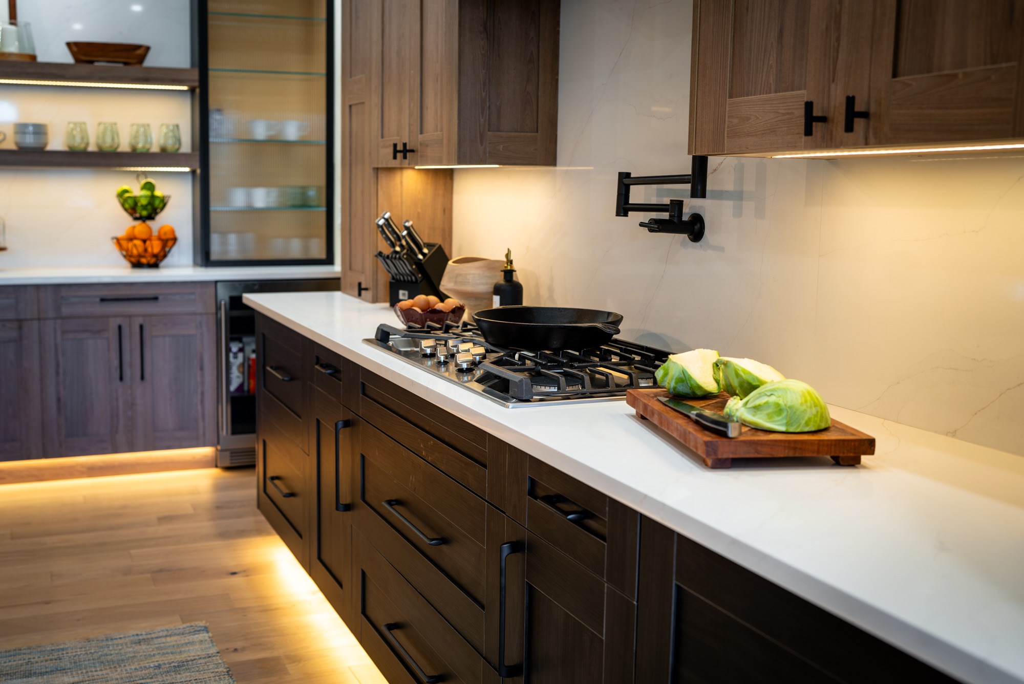 Kitchen with walnut-stained cabinets, a white quartz counter, a pot filler and lit toe kicks