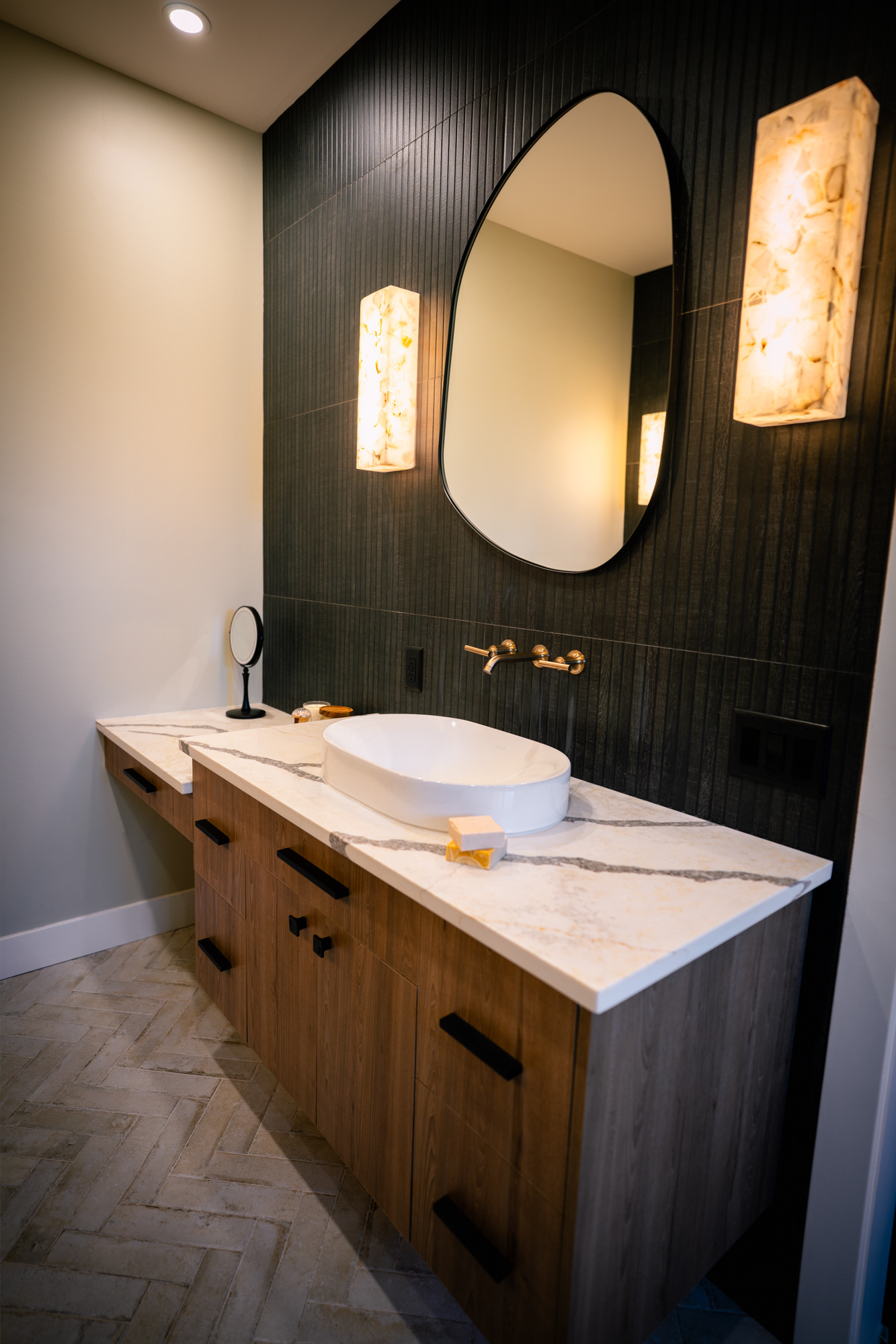 Powder room with a vessel sink, a pebble mirror and alabaster sconces on black fluted tile
