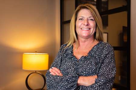 Denise Ward, Administrative Assistant at Perez Design Build Remodel, smiling with arms crossed in an office setting, showcasing her approachable demeanor and professionalism.