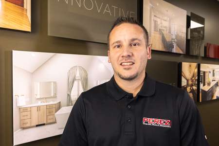 Jason Shifler, Project Manager at Perez DBR, standing in front of design displays, wearing a black polo shirt with the Perez logo, showcasing expertise in cabinetry and trim work.