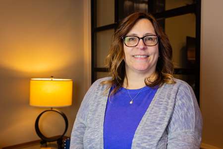 Lynn Moretti, Office Manager at Perez DBR, smiling in a professional setting with a lamp in the background, representing her role in managing company operations since 2003.