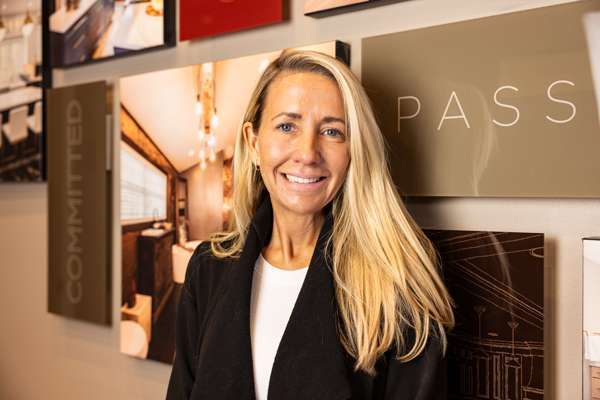 Kolia Perez, New Customer Acquisition and Customer Service specialist at Perez Design Build Remodel, smiling in front of a wall featuring design elements and the word "PASSION."