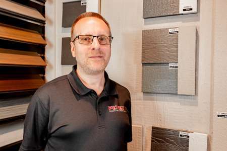 Michael Woods, Project Consultant at Perez DBR, standing in front of material samples showcasing various textures and colors relevant to remodeling projects.